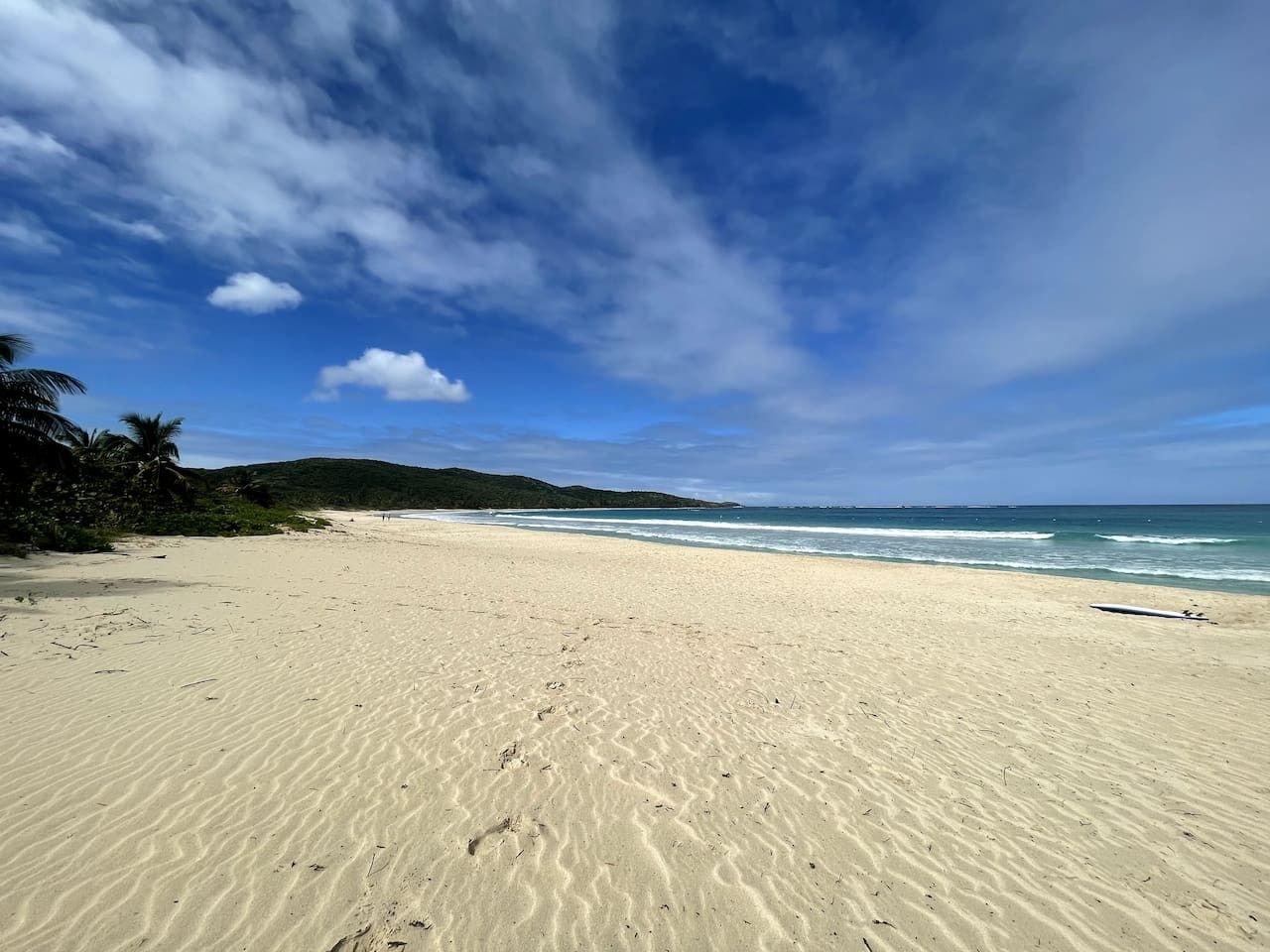 A beach with sand, ocean, and distant hills.