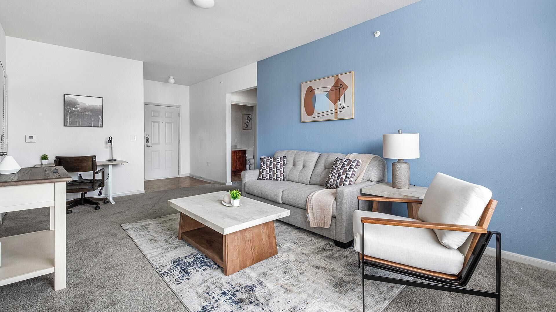 A modern living room with a grey sofa, a wooden coffee table, a white armchair, and a blue accent wall.