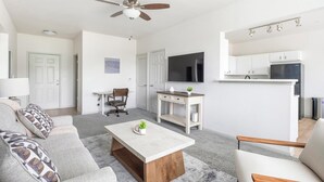 Een moderne woonkamer met een bank, salontafel, televisie en een keukenhoek met kastjes en een magnetron.