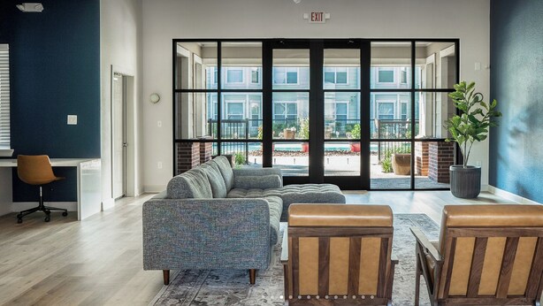 Een modern interieur met een modulaire bank, twee leren fauteuils, een potplant en uitzicht door grote glazen deuren op een buitenruimte.