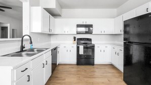 Een moderne keuken met witte kasten, een zwarte koelkast, roestvrijstalen apparatuur en een houten vloer.