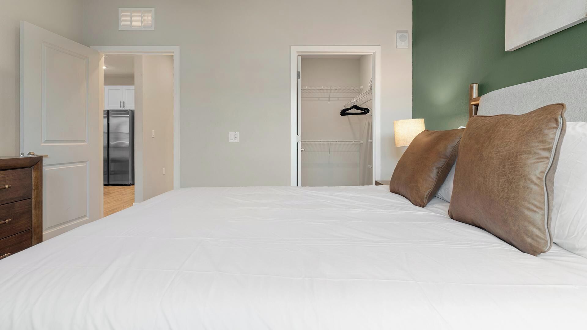 Een slaapkamer met een bed, een kledingkast, een hangende kledingrek en een deur naar een keuken.