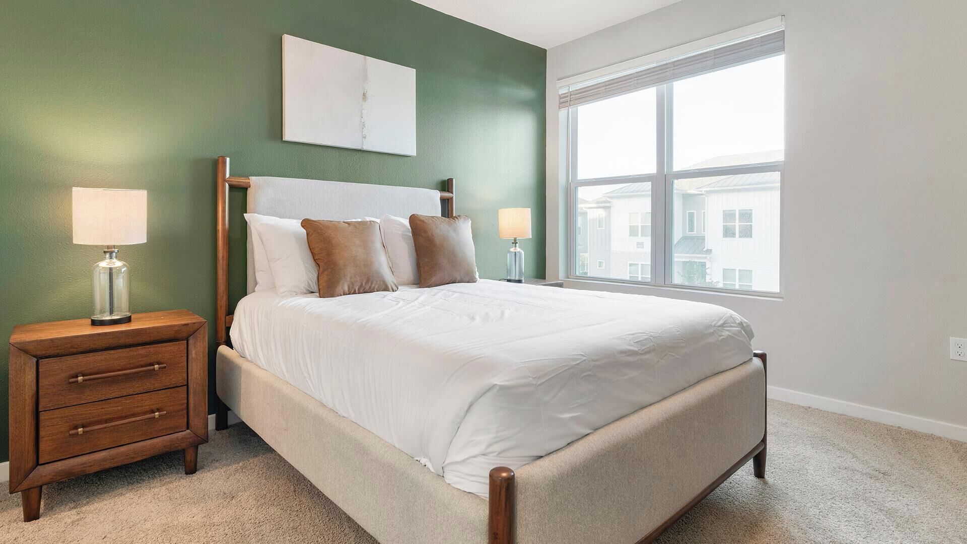 Een slaapkamer met een bed, nachtkastjes, een raam en uitzicht op gebouwen.