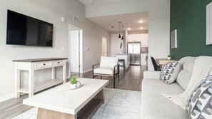 Ein modernes Wohnzimmer mit Flachbildfernseher, Essbereich und einer Küche im Hintergrund.