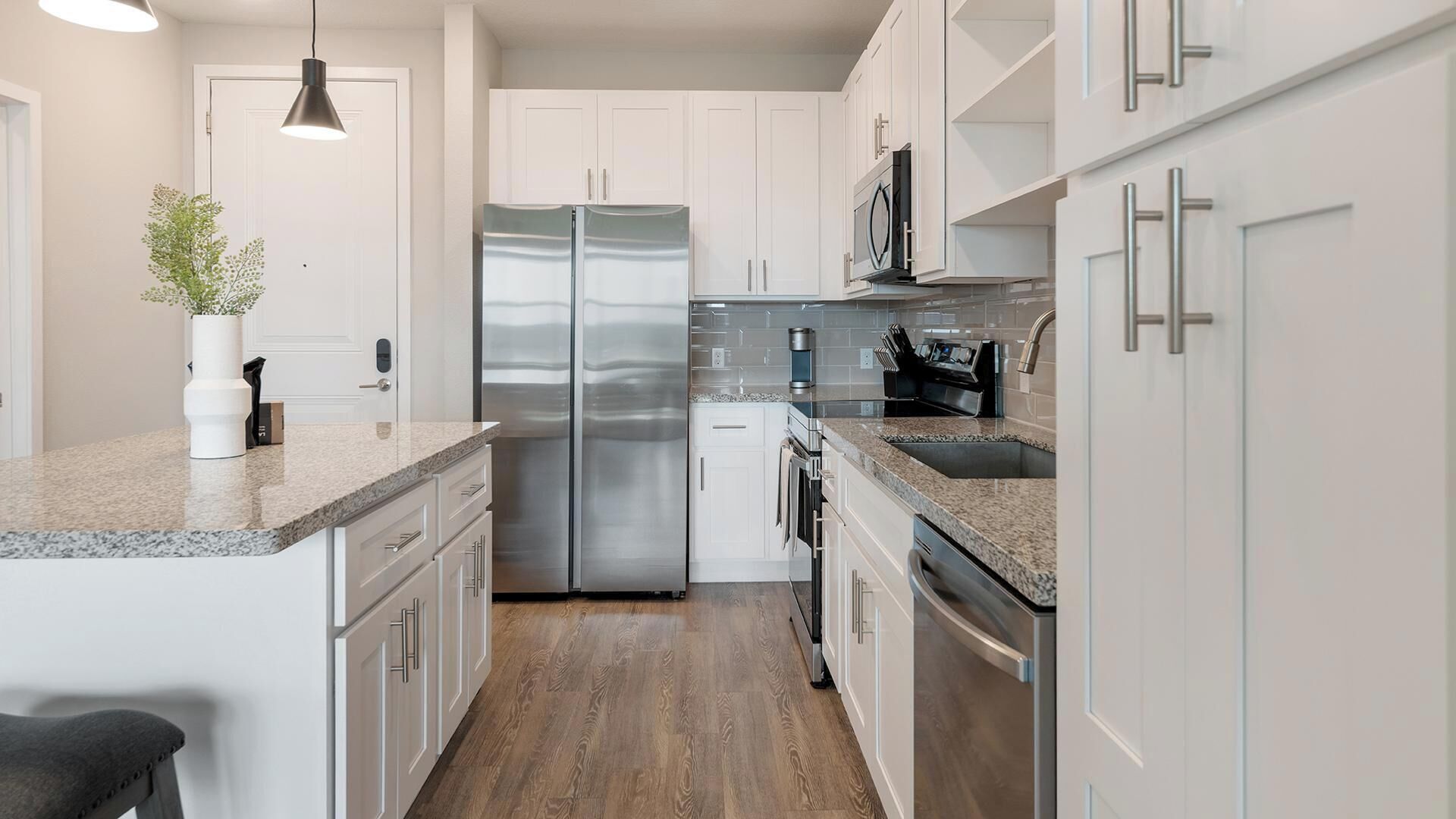 A modern kitchen with white cabinets, stainless steel appliances, and a granite countertop.