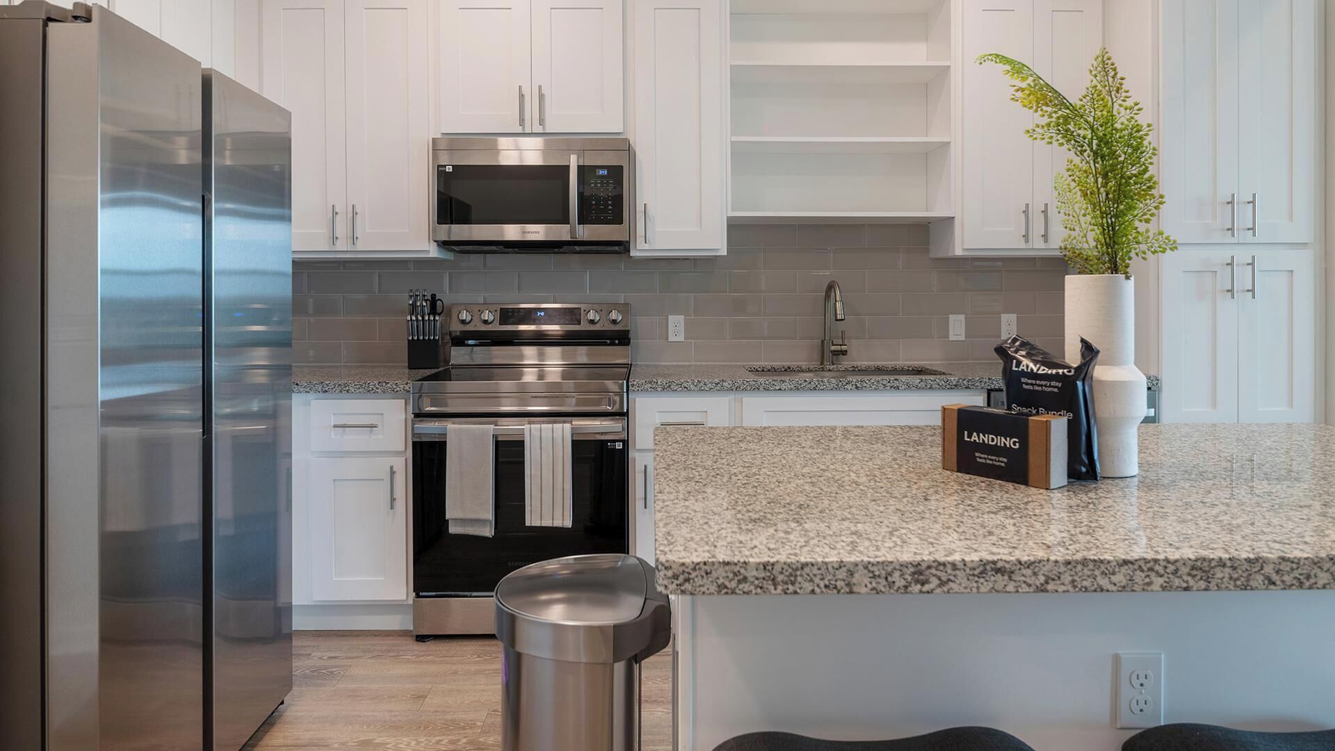 A modern kitchen with stainless steel appliances, white cabinetry, and a granite countertop.