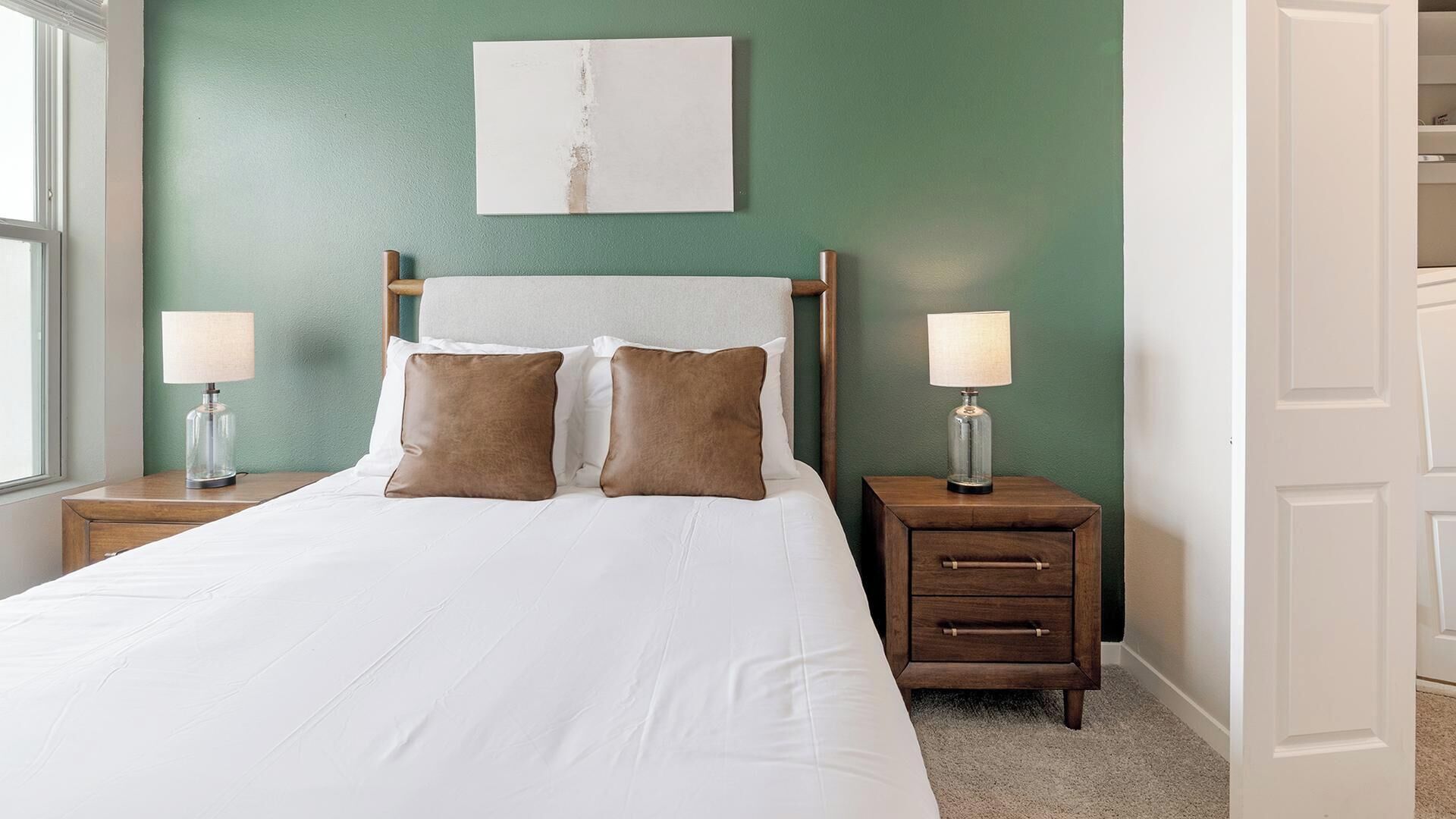 A neatly made bed with two pillows, a bedside table with a lamp, and a nightstand with a lamp.