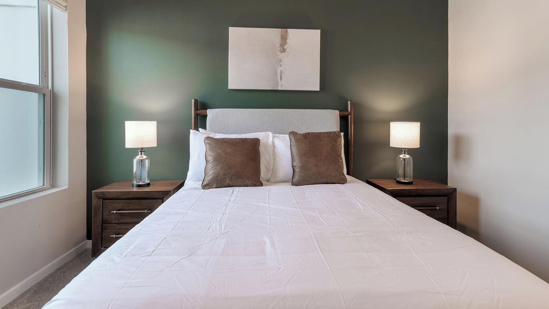 Une chambre d’hôtel avec un grand lit, deux tables de chevet avec des lampes, une tête de lit et un tableau au mur.