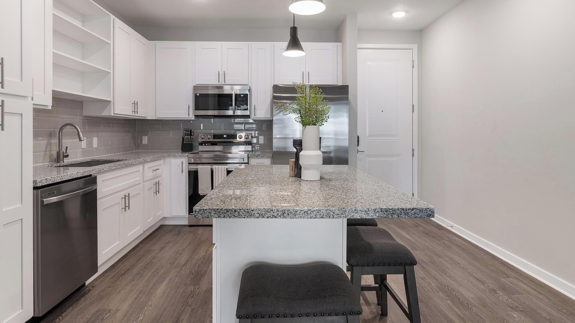 A modern kitchen with white cabinets, stainless steel appliances, a granite countertop, and a central island with bar stools.