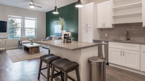A modern kitchen with white cabinets, a granite countertop, a stainless steel dishwasher, and a bar area with stools. - Landing | Stylish 1BD, Yoga Studio, Gym (Four Corners)