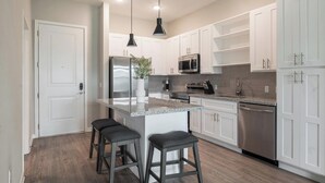 A modern kitchen with white cabinetry, stainless steel appliances, a granite countertop, and two bar stools. - Landing | Spectacular 1BD, Yoga Studio, Gym (Four Corners)