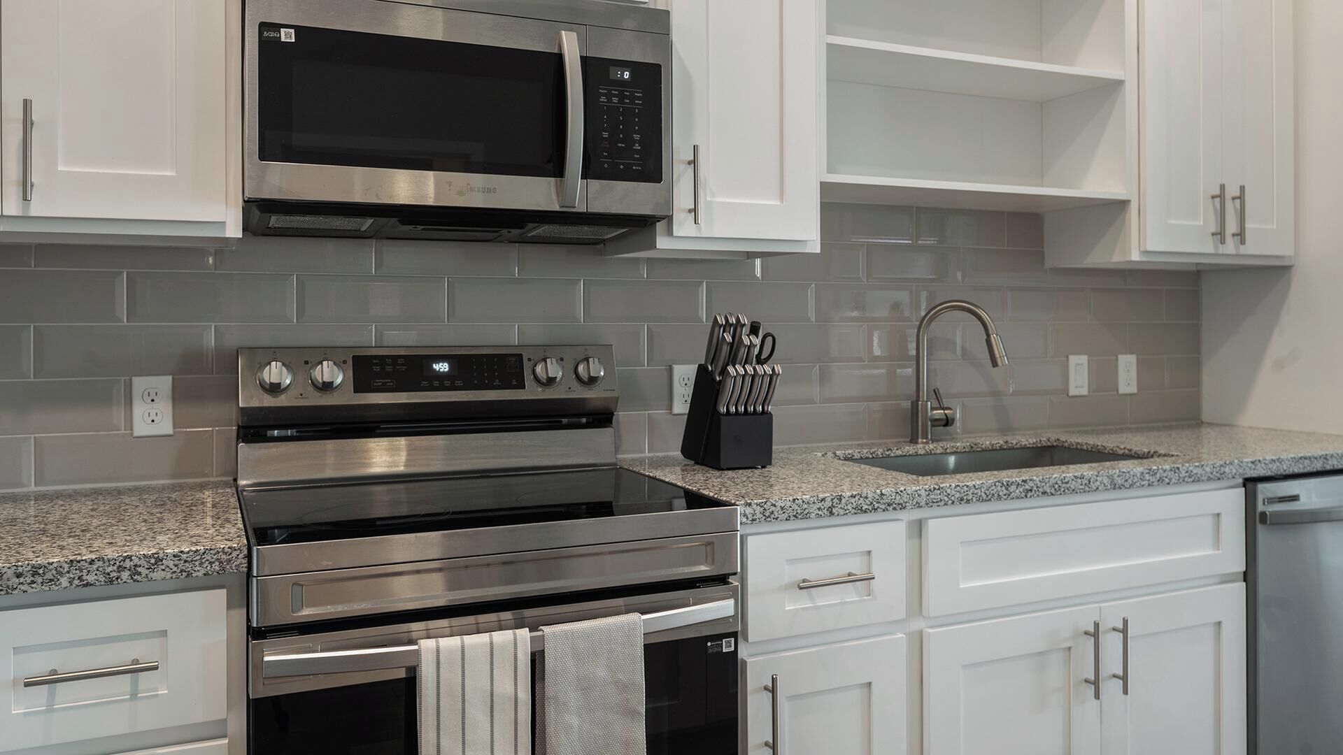 A kitchen with stainless steel appliances, white cabinets, a granite countertop, and a knife block.