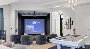 A modern room with a pool table, comfortable seating, a projector screen displaying a golf game, and a fire extinguisher on the wall. - Landing | Spectacular 1BD, Yoga Studio, Gym (Four Corners)