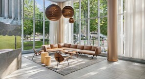 A modern lounge with a leather sofa, round wooden tables, and large windows offering a view of the outdoors. - Landing | Spectacular 1BD, Gym (Washington)