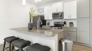 A modern kitchen with granite countertops, stainless steel appliances, and a small island with bar stools. - Landing | Stunning 1BD, Game Room (Lake Wales)