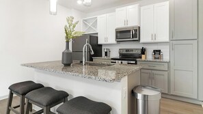 A modern kitchen with granite countertops, stainless steel appliances, and a small island with bar stools.