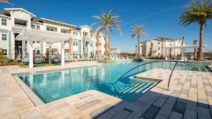 A swimming pool with a 6 ft depth marker, lounge chairs, palm trees, and a building with balconies. - Landing | Stunning 1BD, Game Room (Lake Wales)