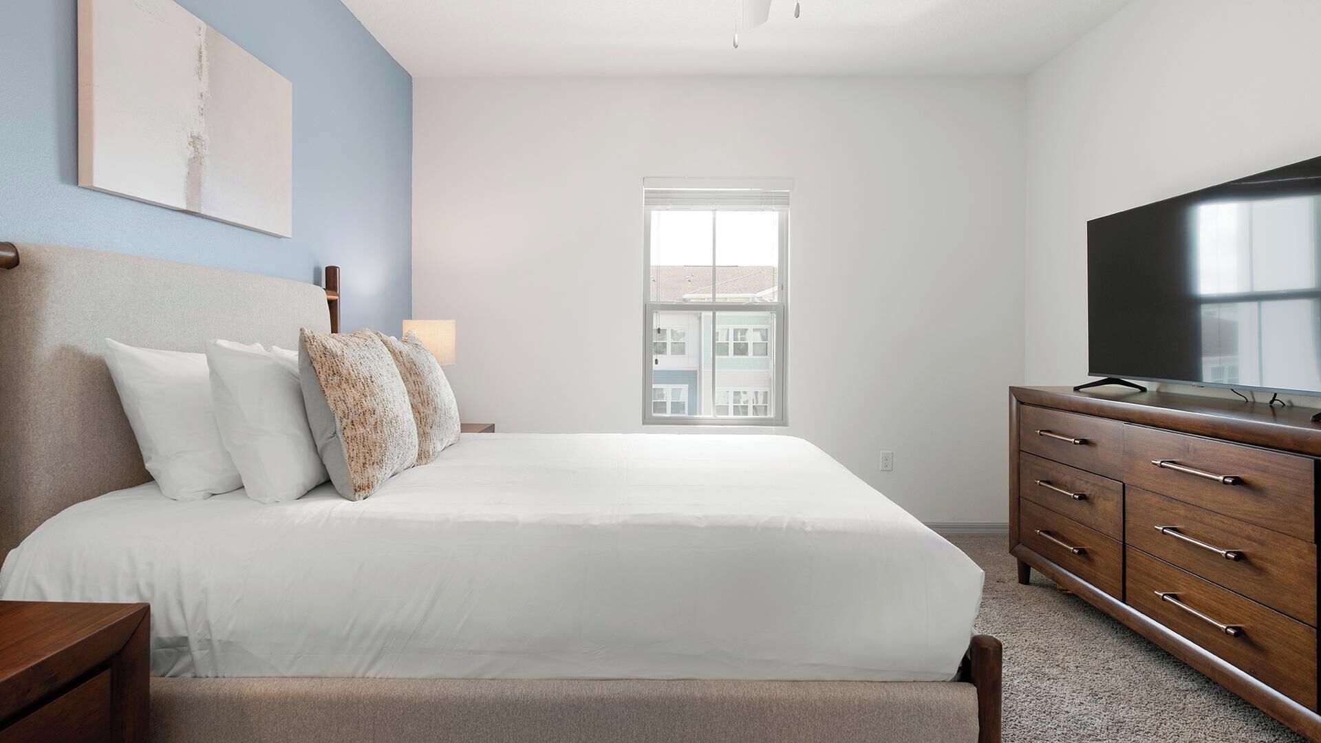 A bedroom with a bed, a dresser, a television, and a window.
