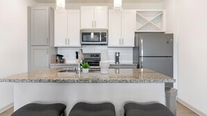 Une cuisine moderne avec des meubles blancs, un comptoir en granit, des appareils en acier inoxydable et un coin bar avec des tabourets.