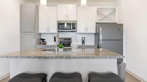A modern kitchen with white cabinets, a granite countertop, stainless steel appliances, and a bar stool area.