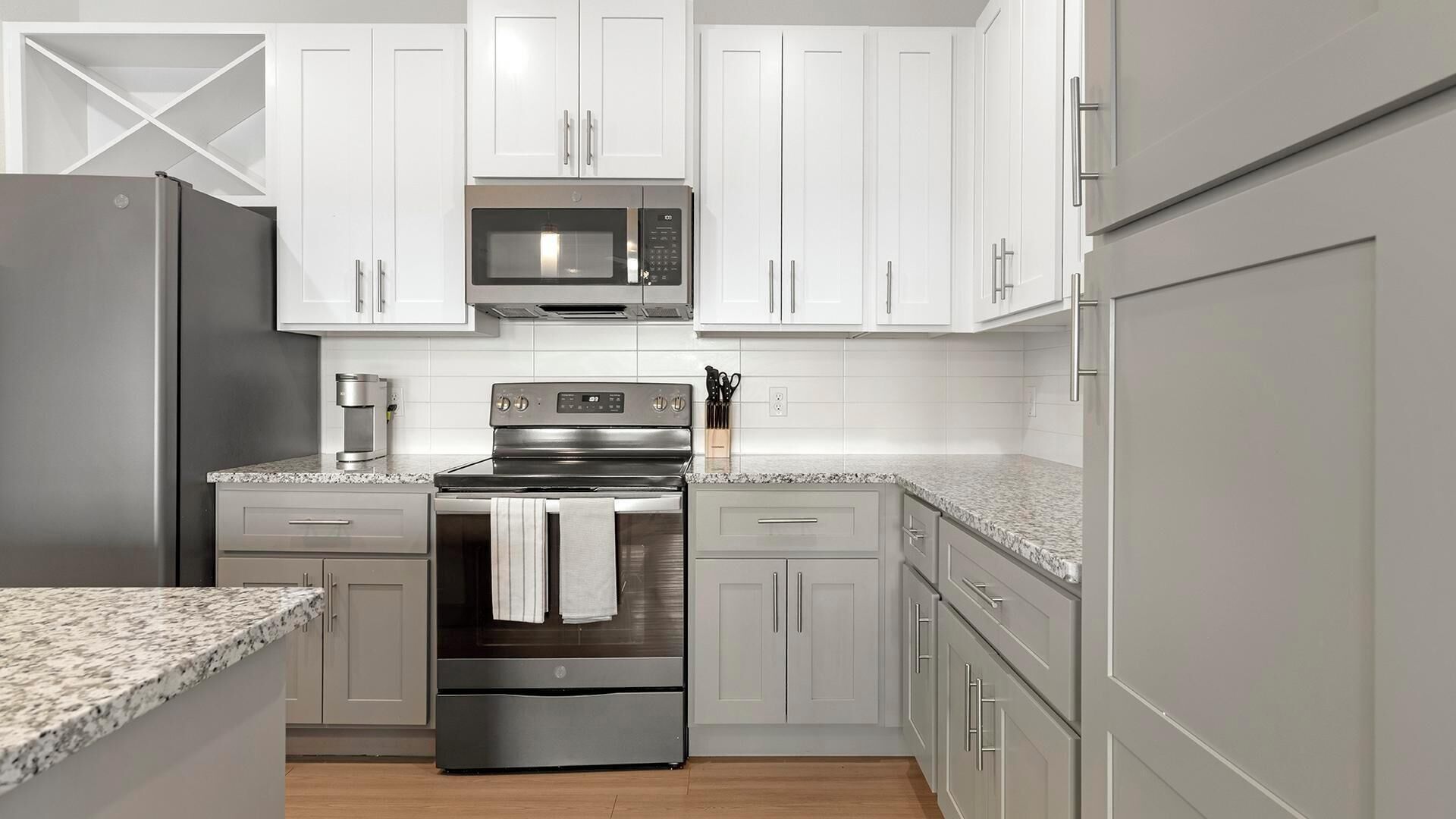 A modern kitchen with stainless steel appliances, white cabinetry, and a granite countertop.