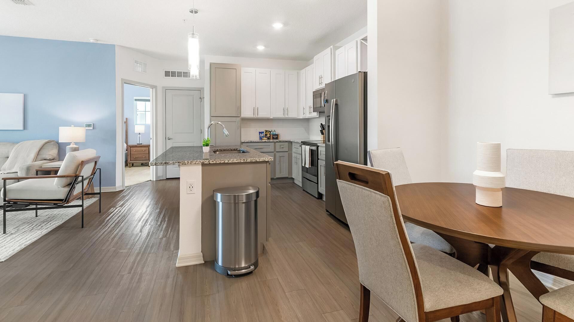 A modern kitchen with white cabinets, a stainless steel refrigerator, and a dining area with a wooden table and chairs.