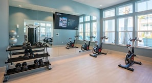 A gym with exercise bikes, dumbbells, and a large mirror.