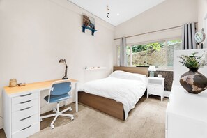 Een slaapkamer met een bed, bureau, stoel en een raam met uitzicht op groen.