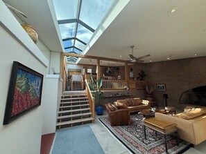 En rummelig opholdsstue med højt til loftet, trappe og pejs.