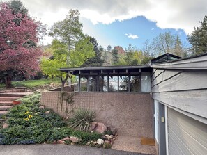 Een huis met een overdekte patio, een tuin vol planten en uitzicht op het omliggende landschap.