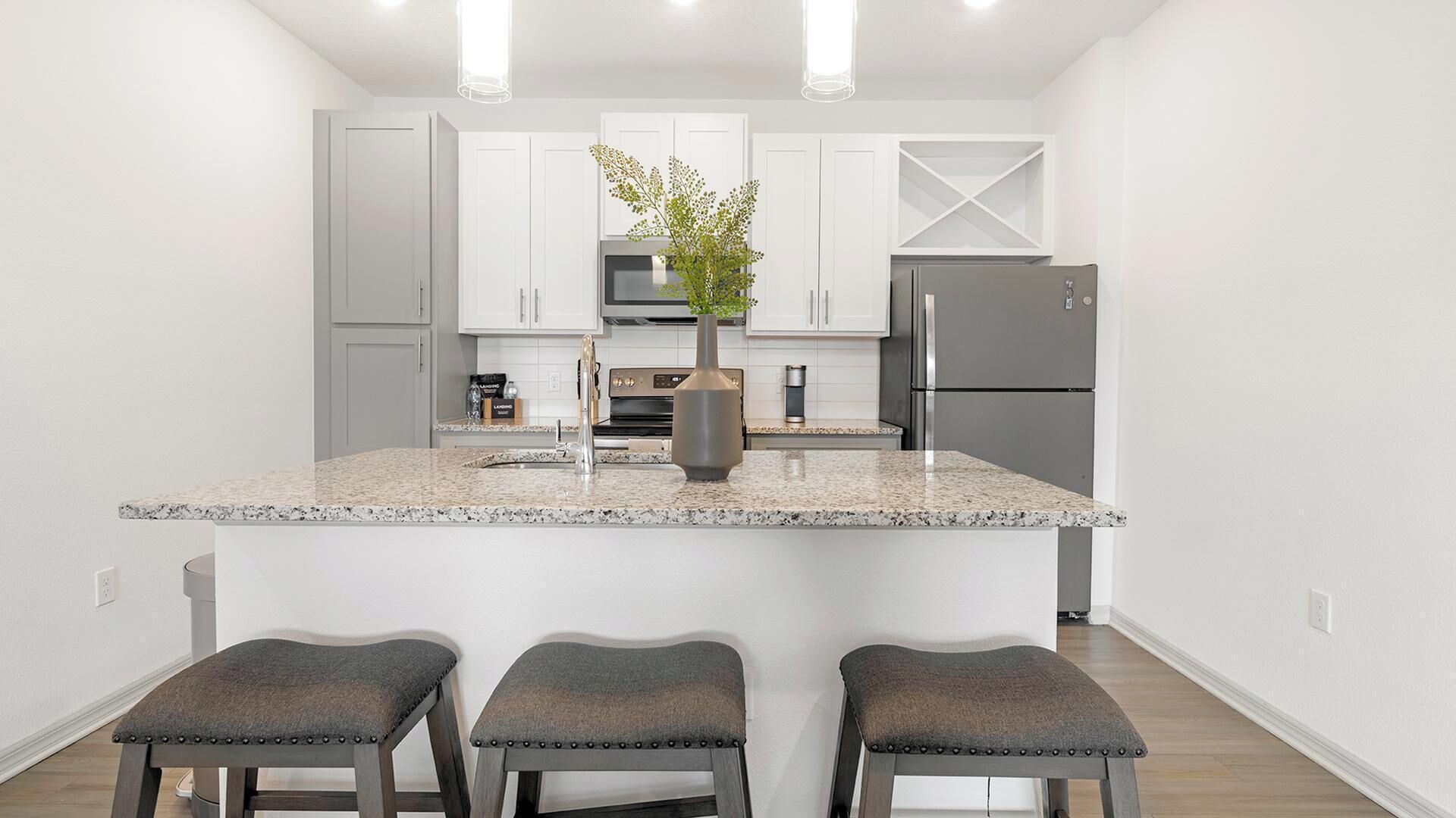 A modern kitchen with a central island, white cabinetry, stainless steel appliances, and a vase with greenery.