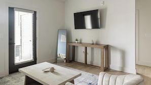A modern living room with a flat-screen TV mounted on the wall, a wooden console table, a white sofa, and a marble coffee table. - Landing | Chic 1BD, Gym, Clubhouse (Asheville)
