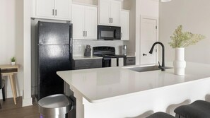 A modern kitchen with white cabinets, a black refrigerator, a microwave, a stove, and a sink. - Landing | Beautiful 1BD, Clubhouse, Gym (Asheville)