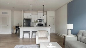 A modern kitchen with white cabinetry, a central island, and a dining area with a sofa and chairs. - Landing | Beautiful 1BD, Clubhouse, Gym (Asheville)