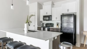 A modern kitchen with white cabinets, a black refrigerator, a microwave, and a stove. - Landing | Stylish 1BD, Gym, Clubhouse (Asheville)