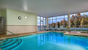 Una piscina interior con paredes de vidrio transparente, un reloj y vistas a árboles.