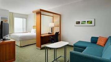 A hotel room with a bed, desk, chair, television, and a sofa.