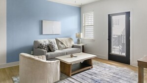 A living room with a grey sofa, a small table, a chair, a lamp, and a door with blinds. - Landing | Incredible 1BD, Gym, Clubhouse (Asheville)