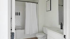 Une salle de bain avec des toilettes blanches, un rideau de douche, un lavabo blanc avec un miroir et un tableau encadré au mur.