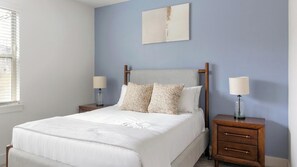 Une chambre à coucher avec un lit, deux tables de chevet avec des lampes, une tête de lit et un tableau au mur.