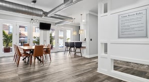 A modern game room with a wooden table, chairs, a TV, and a wall-mounted rule sign. - Landing | Chic 2BD, Pool, Gym (Dallas)