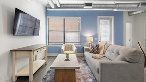 Ein Wohnzimmer mit Fernseher, Sofa, Sessel, Couchtisch und Lampe.