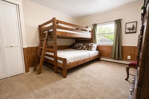 A bunk bed with a ladder, a window with curtains, a door, and a wall-mounted picture.