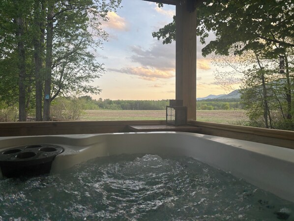 A hot tub under a wooden pergola with a view of a field and trees.