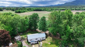 A white house with a blue roof surrounded by lush greenery and a mountainous backdrop.