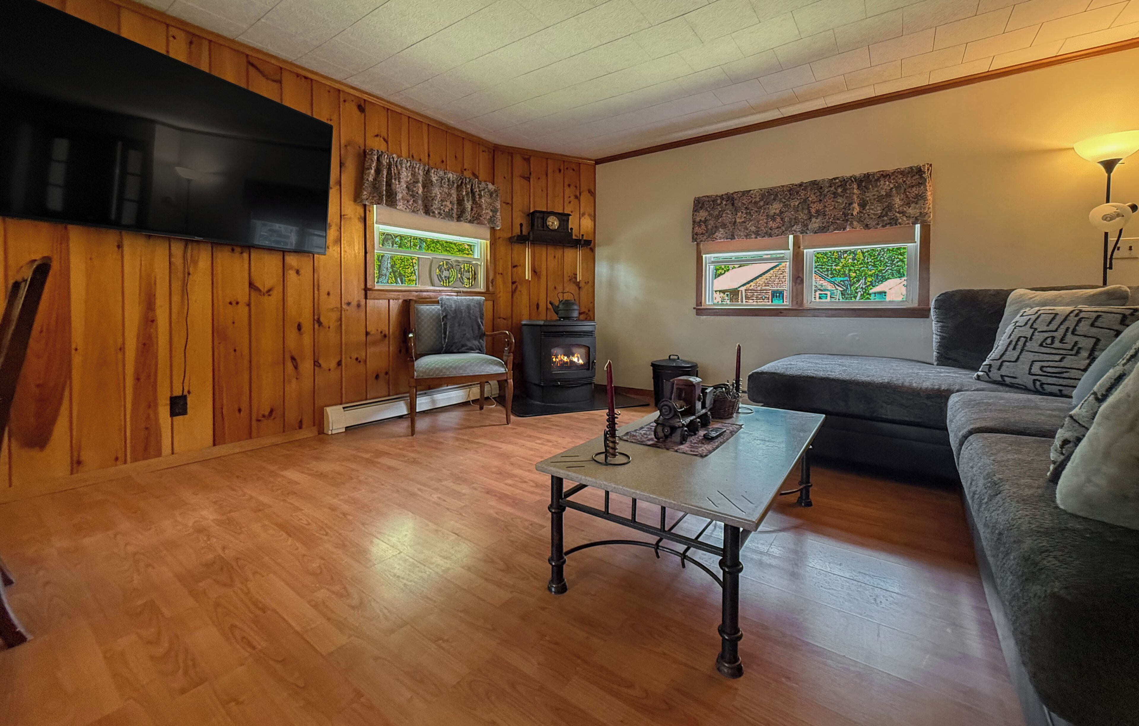 Una habitación acogedora con pared revestida de madera, televisor de pantalla plana, sofá, una mesa con un objeto decorativo y estufa de leña.