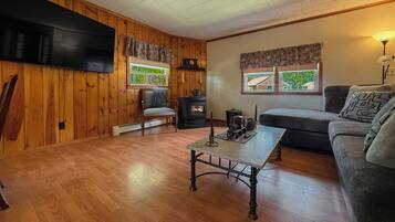 Una habitación acogedora con pared revestida de madera, televisor de pantalla plana, sofá, una mesa con un objeto decorativo y estufa de leña.