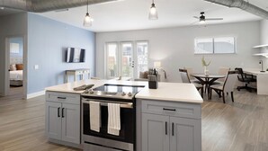 A modern kitchen with a central island, a dining area with a round table, and a living space with a TV. - Landing | Incredible 2BD, Courtyard, Clubhouse (Dallas)