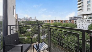 A balcony with a metal railing, a black woven chair, and a glass table. - Landing | Incredible 2BD, Courtyard, Clubhouse (Dallas)
