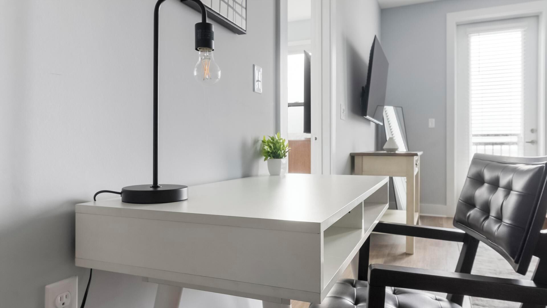 Ein moderner Schreibtisch mit Lampe, Stuhl, Topfpflanze und Fernseher an der Wand.